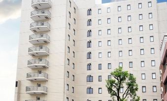 a large white building with multiple floors , possibly a hotel or office building , surrounded by trees and other buildings at Hotel Resol Machida