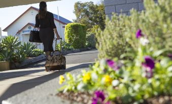 a woman is walking down a sidewalk next to a flower bed , carrying a suitcase and a handbag at Gatton Motel