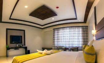 a hotel room with a comfortable bed , white curtains , and a yellow bed runner , as well as a dining table and chairs at The Fern Residency Vijayapura