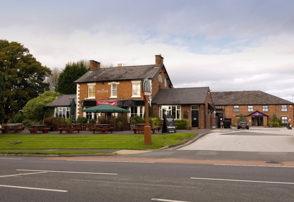 a brick building with a large sign on the front , surrounded by trees and grass at Premier Inn Crewe (Nantwich)