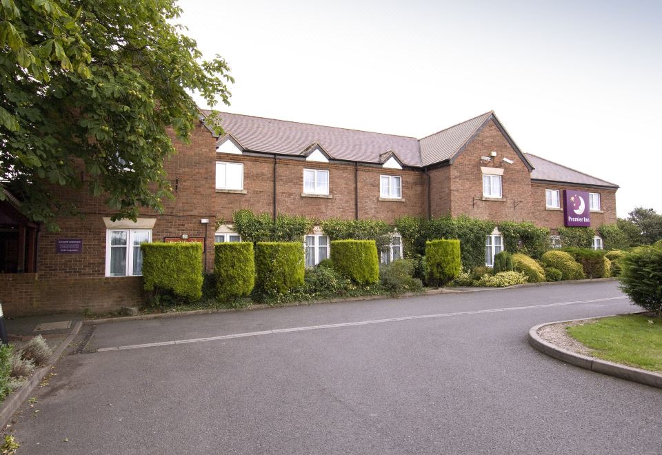 a brick house with a paved walkway in front of it , surrounded by trees and bushes at Premier Inn Lichfield North East (A38)