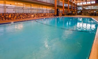 an indoor swimming pool with clear blue water , surrounded by stone walls and wooden fencing , in a hotel building at Best Western State Fair Inn