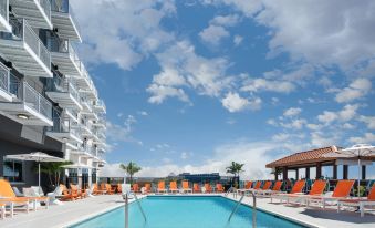 a large swimming pool with orange lounge chairs and a white building in the background at Aloft Ocean City
