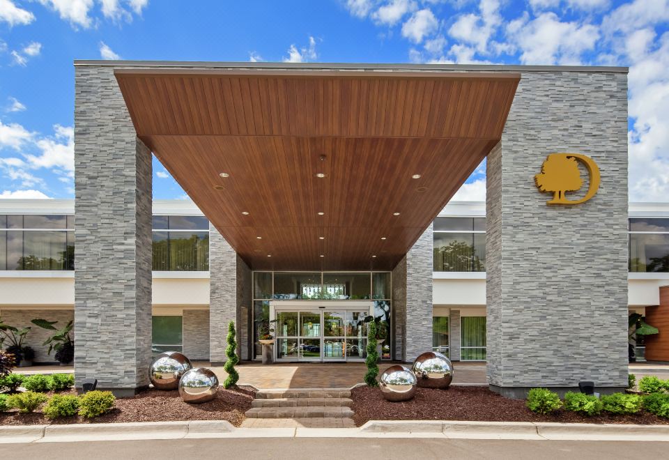 the exterior of a large building , possibly a hotel , with a large entrance and several potted plants at The Kingsley Bloomfield Hills - a DoubleTree by Hilton