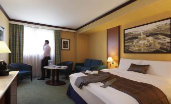 a hotel room with a king - sized bed , a man sitting on the bed , and a woman standing near the window at Mercure Versailles Paris Ouest