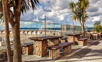 a group of stone benches lined up on a sidewalk next to a fence , with palm trees and a body of water in the background at Radisson Blu Waterfront Hotel, Jersey