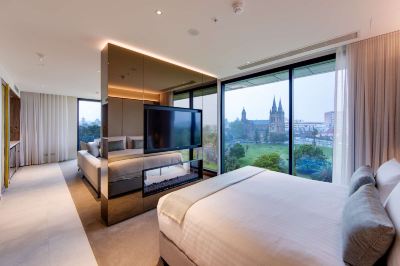 a luxurious bedroom with a king - sized bed and a large flat - screen tv mounted on the wall at Oval Hotel at Adelaide Oval, an EVT hotel