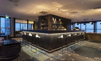 a modern bar with a black counter and black chairs , surrounded by windows offering views of the ocean at Scandic Narvik