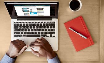 a man is sitting at a desk with a laptop , working on a project , and holding a pen at Hilton Garden Inn Irvine Spectrum Lake Forest