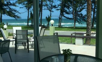 a patio with tables and chairs , a view of the ocean , and trees in the background at Greenseaviewresort Bangsaphan