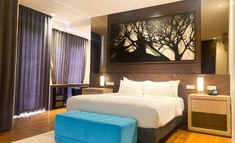 a modern bedroom with a large bed , blue ottoman , and a painting of a tree on the wall at Bromo Park Hotel Probolinggo