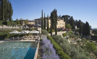 a large villa surrounded by lush greenery , with a swimming pool and umbrellas in the foreground at Rosewood Castiglion del Bosco