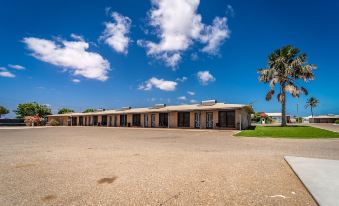 a large , empty parking lot with multiple rows of houses and palm trees in the background at Carnarvon Motel