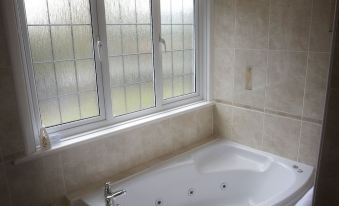 a large , white bathtub is situated in front of a window with frosted glass at Little Silver Country Hotel