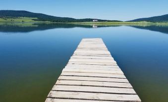 a wooden pier extends into a calm lake , with green hills and trees in the background at Laguna Beach Club Bazaleti Lake