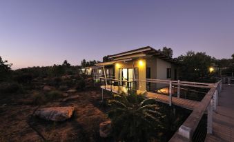 a modern , two - story house with a wooden deck and solar panels , surrounded by rocks and trees at dusk at Groote Eylandt Lodge