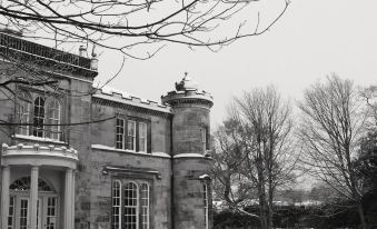 a black and white photo of a large building with snow on the ground and a tree in the background at Kincaid House Hotel