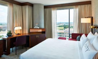a hotel room with a large bed , a desk , a chair , and a window overlooking a cityscape at Renaissance Dallas at Plano Legacy West Hotel