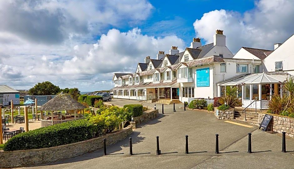 a large white house with a blue sign on the front , surrounded by a parking lot at Trearddur Bay Hotel