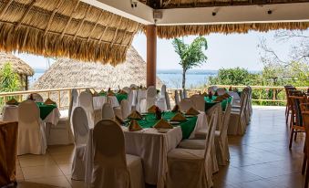 a tropical - themed restaurant with thatched roofs , green tablecloths , and white chairs under a thatched roof , overlooking the ocean at Camino Real Tikal‎