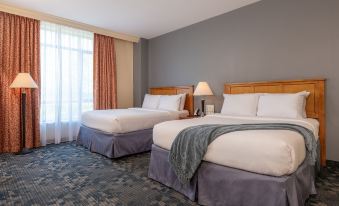 a hotel room with two beds , each made up with white sheets and blue comforters , accompanied by wooden headboards and curtains at Wellsworth Hotel