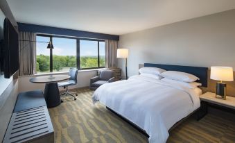 a hotel room with a large bed , a desk , a chair , and a window overlooking a beautiful view at Portland Sheraton at Sable Oaks