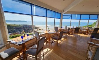 a restaurant with wooden floors and tables , large windows offering ocean views , and lounge chairs around them at Watersmeet Hotel