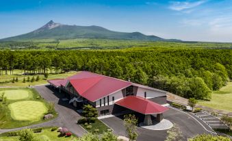 an aerial view of a large building with a red roof , surrounded by lush green trees and mountains in the background at Hakodate-Onuma Prince Hotel