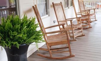a row of wooden rocking chairs is lined up on a porch , with a potted plant in the background at Stonehill's Farmhouse