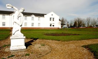 a white building with a statue in front of it , surrounded by a grassy field at Garden Court Hotel Aylesbury