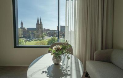 a white table with a vase of flowers sits in front of a window overlooking a cityscape at Oval Hotel at Adelaide Oval, an EVT hotel