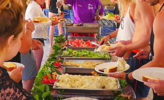a group of people gathered around a long dining table filled with various food items , including fruits , vegetables , and other dishes at Likuri Island Resort Fiji