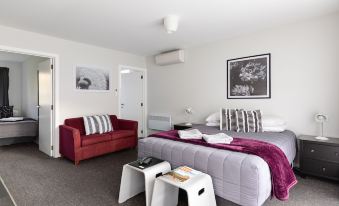 a modern bedroom with a red bed , white couch , and gray and purple furniture , along with some small tables and a framed picture at Arrowtown Motel