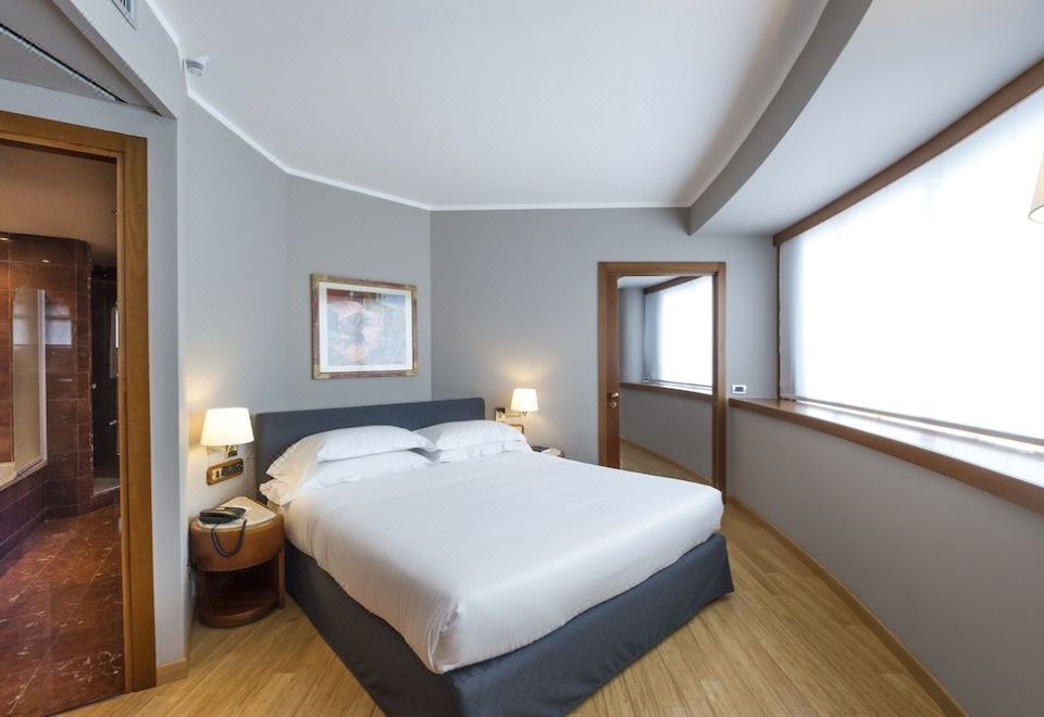 a large bed with white linens is in a room with wooden floors and two lamps on either side of the bed at B&B Hotel Trapani Crystal