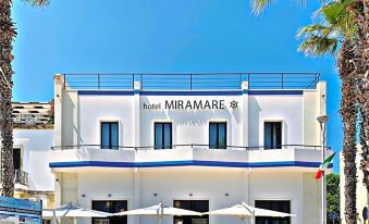 "a white building with the word "" hotel miramare "" on it , surrounded by umbrellas and palm trees" at Hotel Miramare