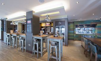 a modern restaurant with a wooden floor , gray booths , and multiple tables and chairs , as well as refrigerators and refrigerators at Premier Inn Honiton