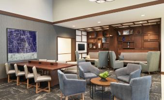 a modern lounge area with blue chairs , wooden tables , and large screens , surrounded by shelves and a bookshelf at Hyatt Place Melbourne / Palm Bay / I-95