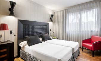 a large bed with a black headboard and white linens is in a room with wooden floors at Salles Hotel Aeroport de Girona