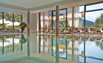 a large indoor swimming pool with multiple rows of chairs and lounge chairs around it at Kempinski Hotel Berchtesgaden