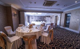 a banquet hall with multiple round tables covered in white tablecloths and adorned with gold sashes at Kings Hotel