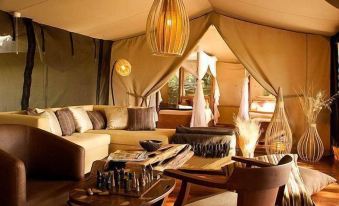 a luxurious tent interior with beige walls , wooden furniture , and various pieces of furniture arranged around the room at Mara Intrepids Tented Camp
