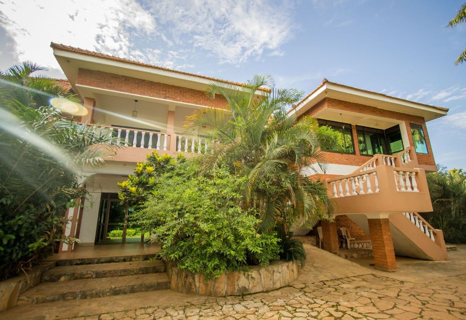 a two - story house with a green lawn , surrounded by trees and bushes , under a blue sky at Hibis Hotel