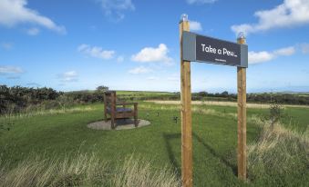 "a wooden bench and a sign with the words "" take a pew "" are standing in a grassy field" at Trenewydd Farm Holiday Cottages