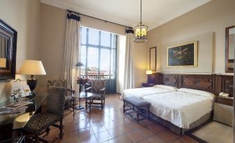 a bedroom with two beds , a chair , and a window overlooking a cityscape through the window at Parador de Lerma