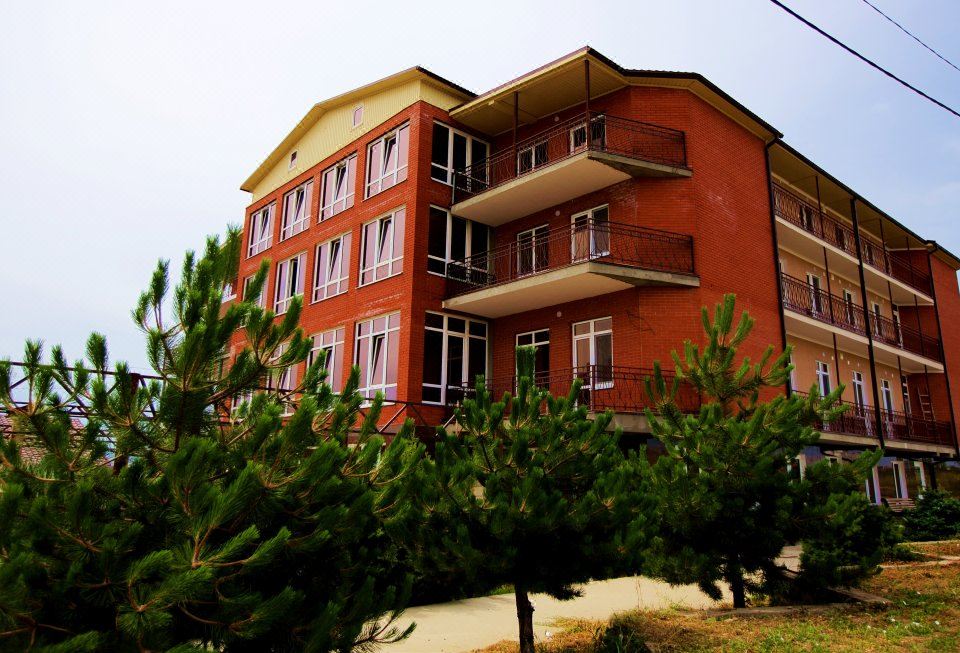a modern red apartment building surrounded by green trees and bushes , creating a picturesque setting at Well Hotel