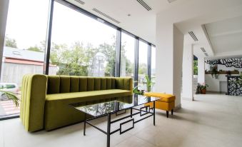 a modern living room with a green couch , yellow ottoman , and glass coffee table in front of large windows at Hotel Avenue - Avenue Hotels