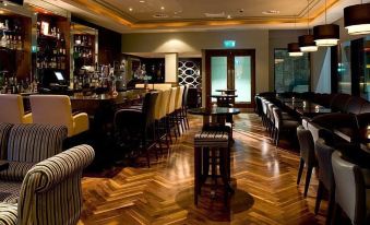 a modern bar with wooden floors , black and white striped chairs , and a long counter at The Savoy Hotel