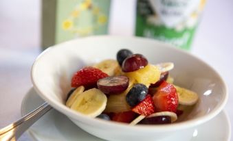 a bowl filled with a variety of fruits , including bananas , strawberries , and blueberries , sits on a dining table at Bridleways Guesthouse & Holiday Homes