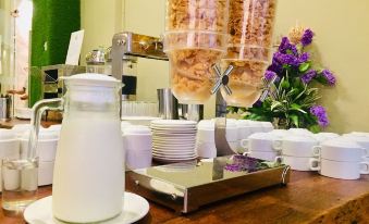 a dining table with a variety of food items and utensils , including bowls , forks , knives , spoons , and cups at Sem9 Senai "Formerly Known As Perth Hotel"