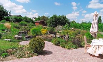 a brick pathway leading to a building surrounded by lush greenery and a pond in the background at La Cote d'Or